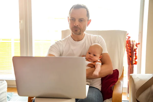 Young man parent working on laptop computer at home office and take care of baby