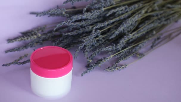 Crema corporal de lavanda y ramo de lavanda sobre fondo violeta, la mujer frota fondos en su mano — Vídeos de Stock