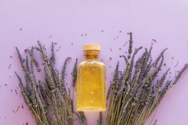 Lavanta yağı, mor arka planda bir şişe ve lavanta buketi.