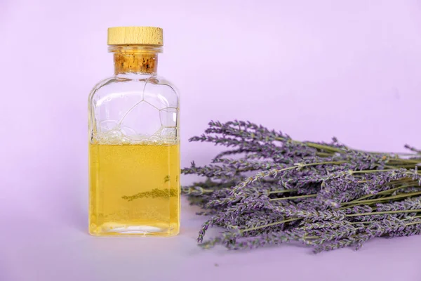 Lavender essential oil, a bottle and lavender bouquet on violet background