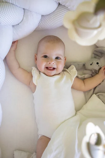 Adorable niña sonriente con un conejito de juguete en la cuna — Foto de Stock