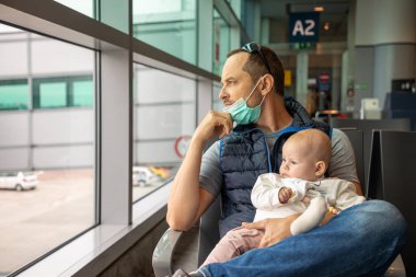 Tıbbi maskeli bir baba ve küçük kızı Prag, Çek Cumhuriyeti, Avrupa havaalanında uçağa binmek için bekliyorlar.