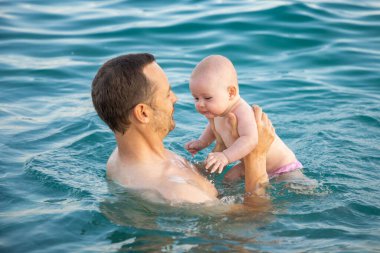 Baba ve kızı gün batımında denizde yüzüyor ve dinleniyorlar. Kızı olan bir adam denizin önünde dinleniyor.