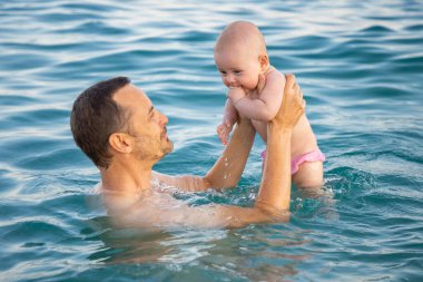 Baba ve kızı gün batımında denizde yüzüyor ve dinleniyorlar. Kızı olan bir adam denizin önünde dinleniyor.