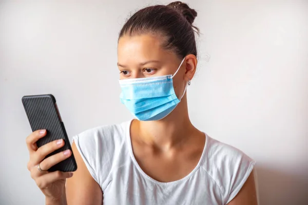 Young woman in medicine mask with smart phone in the hand on white background, medical concept