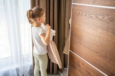 Küçük bir kız aynanın önünde dikiliyor ve elbisesini kendine doğru tutuyor. Kendini ifade etme kavramı, hayal gücü ve giysi ve görünüme erken ilgi. Yüksek kalite fotoğraf