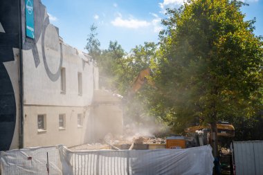 Prag, Çek Cumhuriyeti - 30 Ağustos 2025: Bir şehir caddesinde hidrolik çene ile eski bir binanın parçalarını yıkan yıkım kazıcısı. Yapısal parçalanma ve kentsel yeniden yapılanma kavramı. 