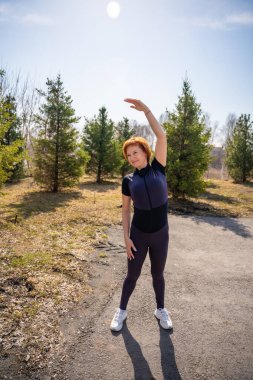 Sabah egzersizi sırasında parkta esneme hareketleri yapan bir kadın. Sağlıklı rutin, vücut hareketliliği ve aktif yaşam tarzı. Yüksek kalite fotoğraf