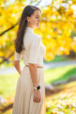 Sonbahar parkında hafif kıyafetli zarif genç bir kadın sonbahar sezonu boyunca Old Money estetiğinden ve klasik tarzından esinlenerek sonsuz moda ve yaşam tarzıyla yürüyor. Yüksek kalite fotoğraf