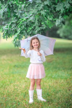 Little girl looking into the camera with joyful eyes while catching raindrops under an umbrella. Engaging with the moment and enjoying the rain through spontaneous play. High quality photo