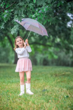 Little girl lifting her umbrella up to the sky and laughing joyfully in the rain. Pure happiness and freedom of movement during a rainy day in the park. High quality photo