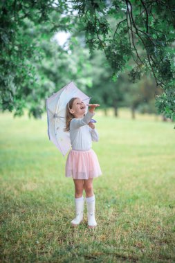 Focus of a child hand reaching out to catch raindrops, with the girl and umbrella softly blurred in the background. A sensory moment focused on nature and touch. High quality photo