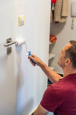 Ev tadilatı sırasında duvarı beyaza boyayan bir adam. İç geliştirme, yüzey dönüşümü ve boya aletleriyle boya çalışması. Yüksek kalite fotoğraf