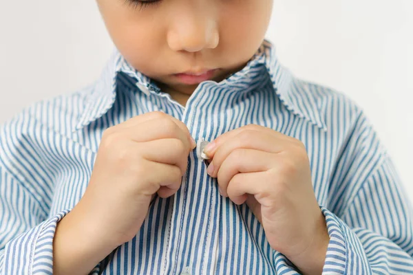 Çocuk gelişimi konsepti: küçük bir anaokulu çocuğunun ellerini kapamak giyinmeyi öğrenmek, çizgili mavi gömleğinin düğmelerini iliklemek. Montessori pratik yaşam becerileri - kişisel bakım, erken eğitim.