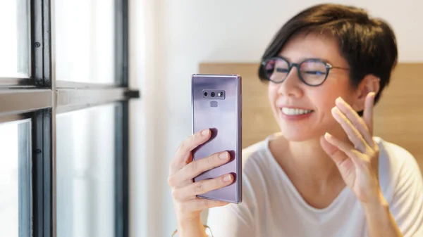 Orta yaşlı güzel bir Asyalı kadın Covid-19 salgını sırasında ailesiyle ve akıllı telefonlu arkadaşlarıyla gülüyor, konuşuyor ve online video görüşmesi yapıyor. Yeni normal, sosyal mesafeleme ve evde kalma kavramı