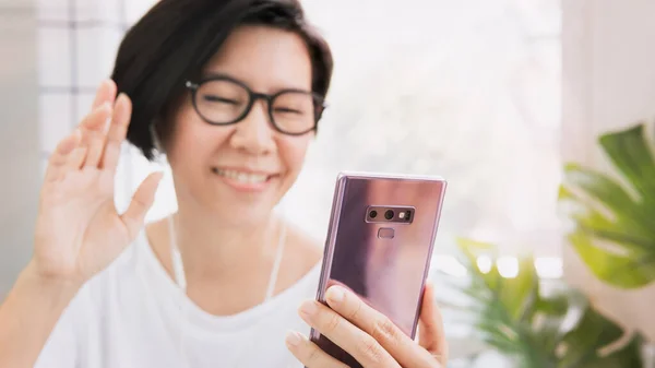 Covid-19 salgını, şehir tecridi, evden ve sosyal mesafelere iş, ev hapsi süresince ev telefonlu güzel orta yaşlı Asyalı kadın gülümsemesi, konuşma ve online video görüşmeleri.