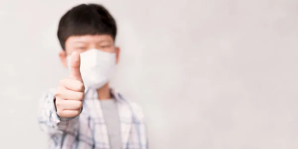 Güvenli ve yeni normal bir konsept olun, genç zeki Asyalı çocuk tıbbi yüz maskesi takın, başparmağınızı kaldırın ve gülümseyerek Coronavirus ve Covid-19 salgınının yayılmasını engelleyin.. 