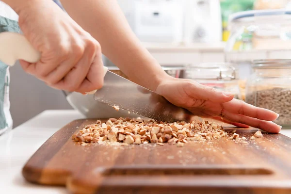 Yakın plan, kadının elleri temiz mutfak masasındaki tahta kesme tahtasında bıçak ve badem (yüksek besin maddeleri, antioksidan ve vitaminler) tutar. Vegan, bitki temelli, vejetaryen ve keto yemeği hazırlama