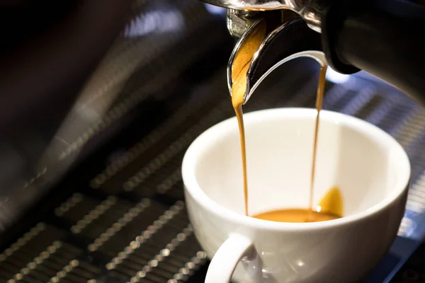 Pompalı espresso makinesi ve iskele filtresi, basınçlı suyu puck 'tan geçirerek demleniyor. Yoğunlaştırılmış kahve akıntısı beyaz seramik fincana dökülür..