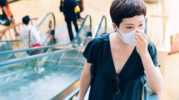 Güzel, orta yaşlı Asyalı kadın öksürük ve ağız kaplıyor, virüs, salgın, grip salgını ve kalabalık ile alışveriş merkezinde salgın hastalıklardan korunmak için tıbbi maske takıyor..