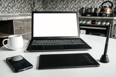 Mutfakta grafik tasarımcı ve mimarın ev işi. Masada dizüstü bilgisayar, grafik tableti ve telefon var. Uzaktan kumanda. Bağımsız