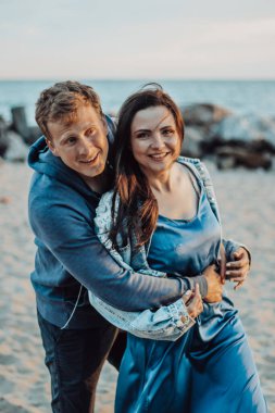  Kumsalda poz veren mutlu yeni evliler. Uzun, dar saçlı mavi elbiseli bir kız ve mavi gözlü bir adam..