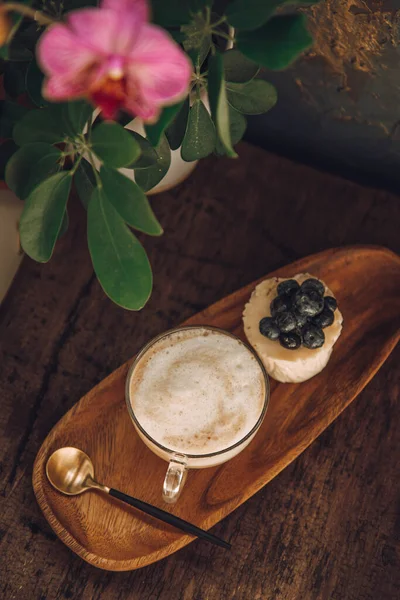 Kaffee mit Milch und ein Kuchen mit Beeren auf einem Holztisch in einem Café. Orchidee schmückt Tisch in Café — Stockfoto