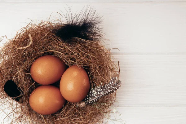 Tři slepičí vejce v hnízdě na bílém dřevěném pozadí. Volné místo pro text — Stock fotografie