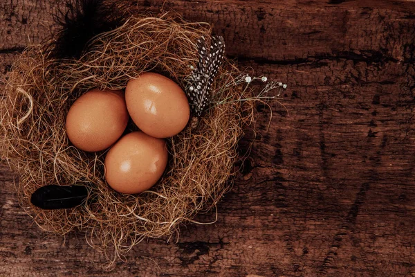 Tři slepičí vejce v hnízdě na hnědém dřevěném pozadí. Rámec pro text — Stock fotografie