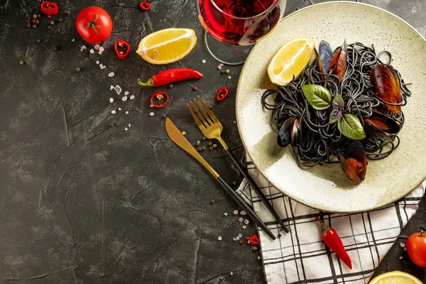 Black pasta with seafood and a glass of red wine on a black background, free space for the text — Stock Photo, Image