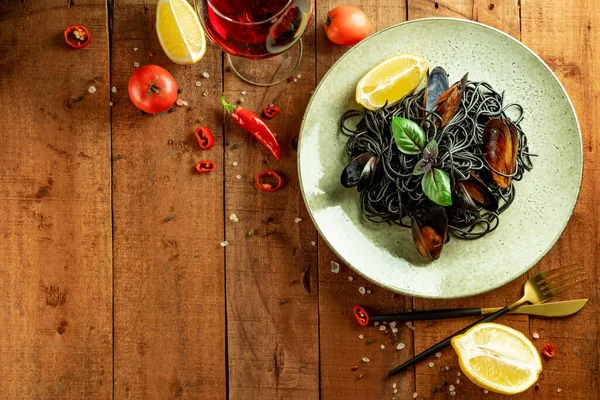 Black pasta with seafood on a plate and wooden background, free space for text — Stock Photo, Image