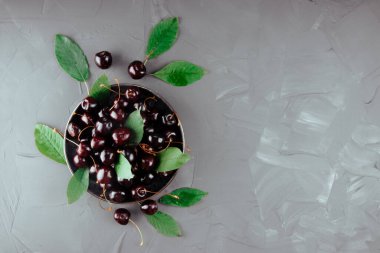 Bir tabak ve beton zemin üzerinde olgun kirazlar, üst görünüm, metin için boş alan