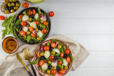 Beyaz ahşap zemin üzerinde kavun, domates ve zeytinli iki porsiyon salata. Metin için boş alan.