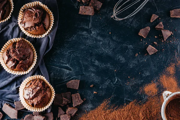 Čokoládové muffiny a kousky čokolády na černém pozadí, volný prostor pro text — Stock fotografie