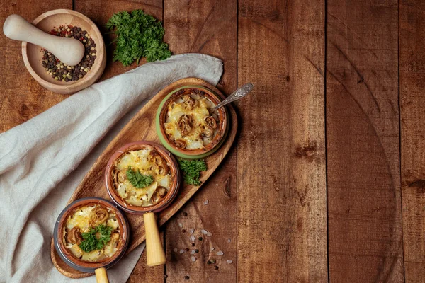  Peynir kabuğunun altında mantarlı fırında patates porsiyonlu tencerelerde ahşap desenli arka planda. Yüksek kalite fotoğraf