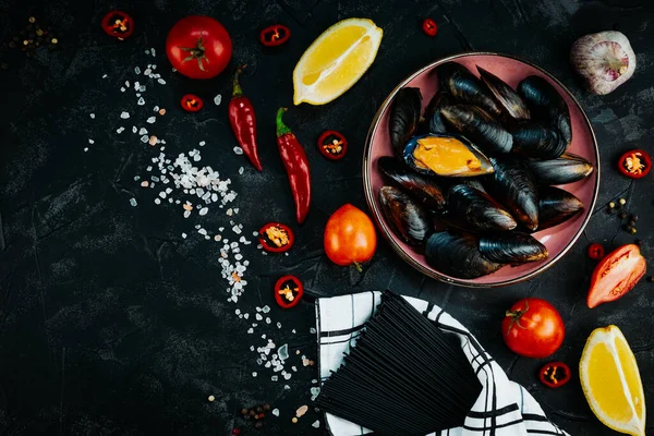Ingredients for cooking pasta with seafood on a black background. Black spaghetti on a wooden background, top view, free space for text. High quality photo