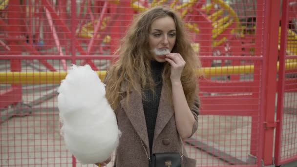 Medium Shot Of Young Adorable Long Hair Curly Blonde Woman In Trendy Coat Enjoying Candy Floss In City Park