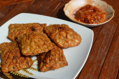 Ahşap masada servis edilen ev yapımı acı biber soslu kızarmış Tempe.