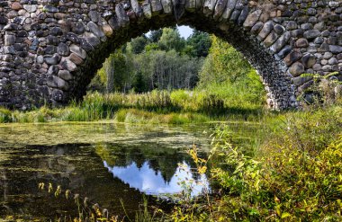 Gökyüzünün yansıması olan eski bir taş köprü kemeri. Vasilevo Malikânesi