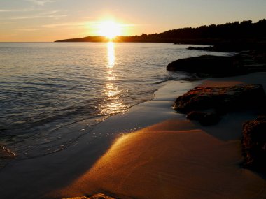 Sıcak güneş ışınları kumlu plaja düşer, adada günbatımı