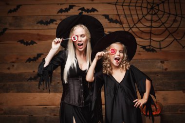 Cadılar Bayramı kavramı - güzel beyaz anne ve kızı cadı kostümleri Cadılar Bayramı Cadılar bayramı şekeri ve tatlı ile yarasalar ve örümcek ağı ahşap studio arka plan üzerinde kutluyor.