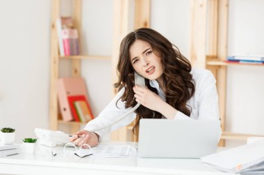 Ofis Masası ve dizüstü bilgisayarını arkasında telefonda konuşurken ciddi iyi giyimli pazarlamacı. Kopya alanı.