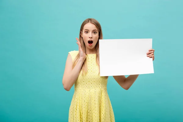 Retrato de cerca, mujer joven en vestido amarillo sosteniendo papel liso blanco con expresión conmocionada por lo que ve, fondo azul aislado . — Foto de Stock