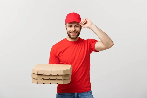 Concetto di consegna: corriere uomo consegna pizza bello in uniforme rossa con tappo contenente scatole di pizza. Isolato su bianco . — Foto Stock
