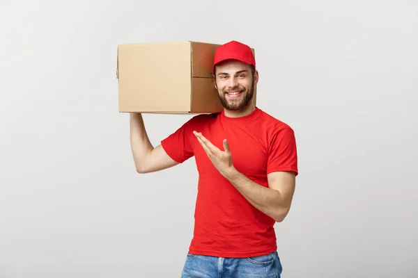 Lieferkonzept - Porträt eines glücklichen kaukasischen Zustellers, der mit der Hand ein Schachtelpaket präsentiert. isoliert auf grauem Studiohintergrund. Kopierraum. — Stockfoto