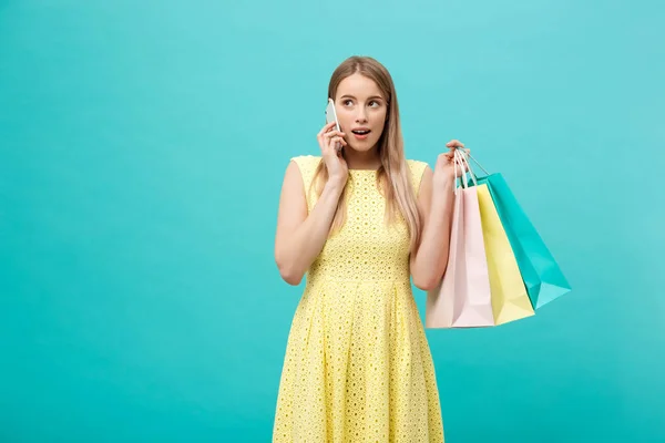 Retrato de mujer caucásica de moda feliz con bolsas de compras llamando en el teléfono móvil. Aislado sobre fondo azul . — Foto de Stock