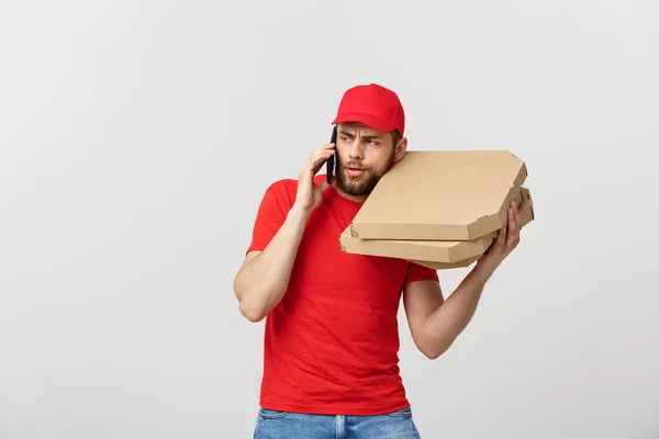 Delivery Concept: Handsome pizza delivery man talking to mobile with shocking facial expression. Isolated over grey background.