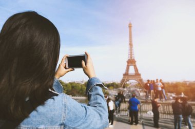 Kadın turist alarak fotoğraf güneş ve mavi gökyüzü altında Paris Eiffel tower yakınındaki telefonla. Dünyanın ünlü popüler bir turistik yer.