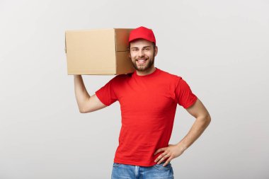 Teslimat Konsepti: genç beyaz yakışıklı teslimatçı omuzunda bir kutu tutuyor. Gri arkaplan üzerinde izole.