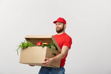 Teslimat kavramı: Yakışıklı teslimat adam bir ağır bakkal kutusu gri arka plan üzerinde izole tutuyor.
